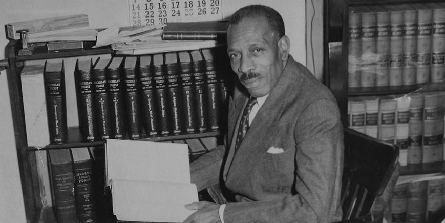 Percy J. Langster reading an open law book next to a bookcase